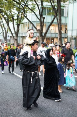 TOKYO, JAPONYA - 27 Ekim 2024 - Japon bir babanın Tokyo 'daki Omotesando Cadılar Bayramı Geçidi sırasında kızının omuzlarında taşıdığı dikey resim.