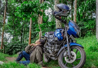 Farklı açılardan çekilmiş motosiklet ve kaskla uzak patikalarda oturan kız yalnız binici yeni yerler keşfetme sevgisini gösteriyor. Görüntü, wayanad kerala Hindistan 'da 10 Mayıs 2020' de çekilmiştir..