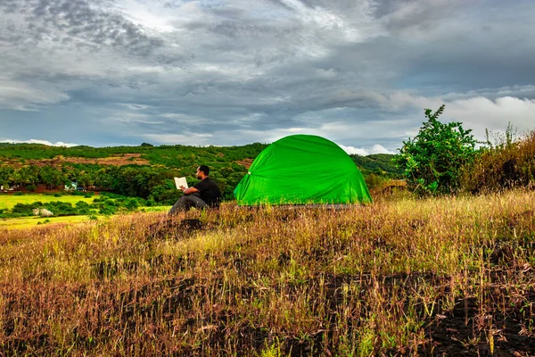 man reading book while camping at mountain top at evening image is taken at gokarna karnataka india. it is showing the human love towards the nature and book reading.