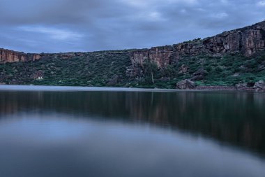 Dağın arka planında el değmemiş göl ve alacakaranlık görüntüsüne uzun süre maruz kalan gökyüzü Agastya Tirtha 'nın Badami Karnataka Hindistan kıyılarındaki Bhutanatha Tapınağı' nın güzelliğini gösteriyor..