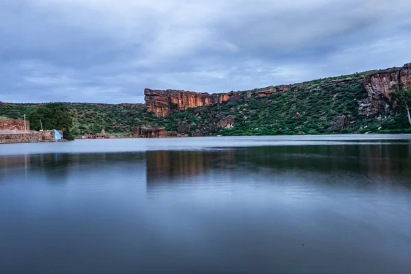 Dağın arka planında el değmemiş göl ve alacakaranlık görüntüsüne uzun süre maruz kalan gökyüzü Agastya Tirtha 'nın Badami Karnataka Hindistan kıyılarındaki Bhutanatha Tapınağı' nın güzelliğini gösteriyor..