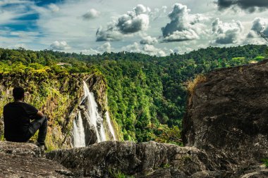 Tepede oturan bir adam akşam görüntüsünde güzel şelaleyi seyrediyor. Jog Falls Karnataka Hindistan 'da çekiliyor. Doğanın güzelliğini gösteriyor..