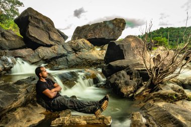 Akşamları çekilen güzel şelale akıntısıyla kayada dinlenen adam uzak batı ghat ormanları Karnataka Hindistan 'da çekiliyor. Doğanın insani sevgisini gösteriyor..