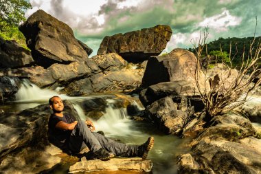 Akşamları çekilen güzel şelale akıntısıyla kayada dinlenen adam uzak batı ghat ormanları Karnataka Hindistan 'da çekiliyor. Doğanın insani sevgisini gösteriyor..