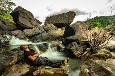 Akşamları çekilen güzel şelale akıntısıyla kayada dinlenen adam uzak batı ghat ormanları Karnataka Hindistan 'da çekiliyor. Doğanın insani sevgisini gösteriyor..
