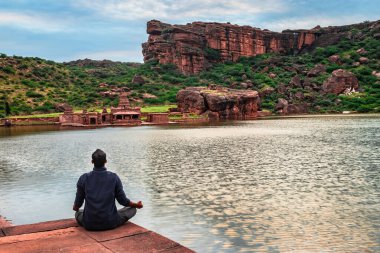 Göl kıyısında, şafak vakti meditasyon yapan bir adam Badami Karnataka Hindistan 'ında Agastya Tirtha sahillerindeki Bhutanatha Tapınağı' nın güzelliğini gösteriyor..