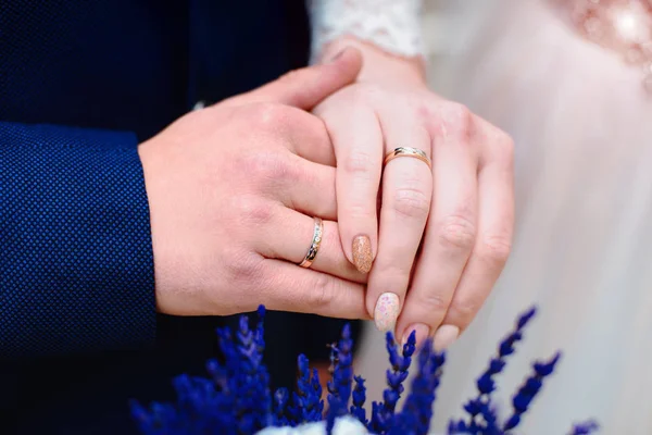 Mains de jeunes mariés avec des anneaux sur des fleurs bleues — Photo