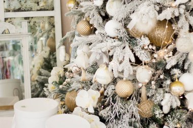 Altın sarısı güzel Noel ağacı, arka planda bulanık ışıklara karşı beyaz dekor, yakın plan