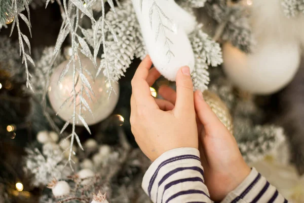 Een kind en een volwassene versieren een kerstboom. Een gouden kerstbal in de hand van een kind. Alle ornamenten wit of goud. — Stockfoto