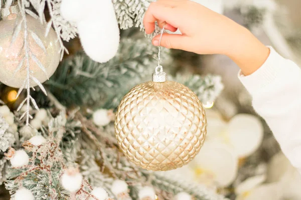 Een kind en een volwassene versieren een kerstboom. Een gouden kerstbal in de hand van een kind. Alle ornamenten wit of goud. — Stockfoto