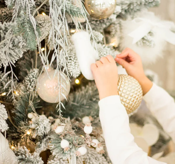 Ein Kind und ein Erwachsener schmücken einen Weihnachtsbaum. eine goldene Weihnachtskugel in der Hand eines Kindes. alle Ornamente weiß oder gold. — Stockfoto