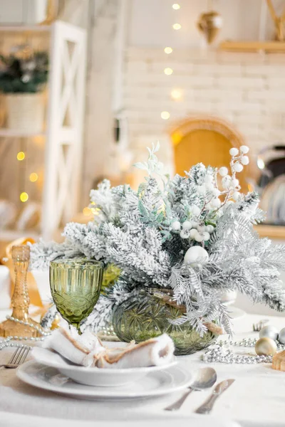 Prachtige serveertafel met decoraties, kaarsen met glazuur op wit tafelkleed op de achtergrond van de keuken met mensen. Woonkamer ingericht met verlichting en kerstboom. — Stockfoto