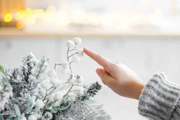 Klein meisje raakt een kerstboom tak met witte bessen op een achtergrond van licht. Kerst- en nieuwjaarsconcept. — Stockfoto