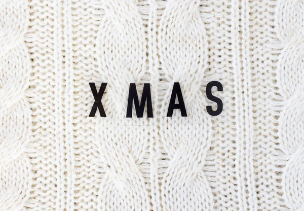 White knitted carpet closeup with the inscription xmas. Textile texture off white background. Detailed warm yarn background. Knit cashmere beige wool.