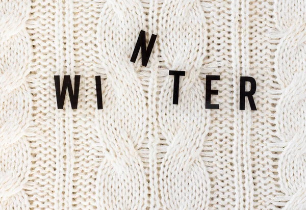 White knitted carpet closeup with the inscription winter. Textile texture off white background. Detailed warm yarn background. Knit cashmere beige wool.