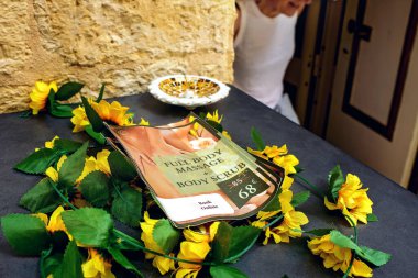 Valletta, Malta - 08.26.2025: Reklam broşürü, sarı çiçekler ve masaj salonu girişinin yanındaki ziyaretçi silueti olan bir masaya yakın çekim.