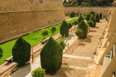 Yürüme yolu, ahşap banklar, yeşil çimenler ve antik taş kale duvarları boyunca budanmış ağaçlar olan iyi korunmuş bir bahçe.
