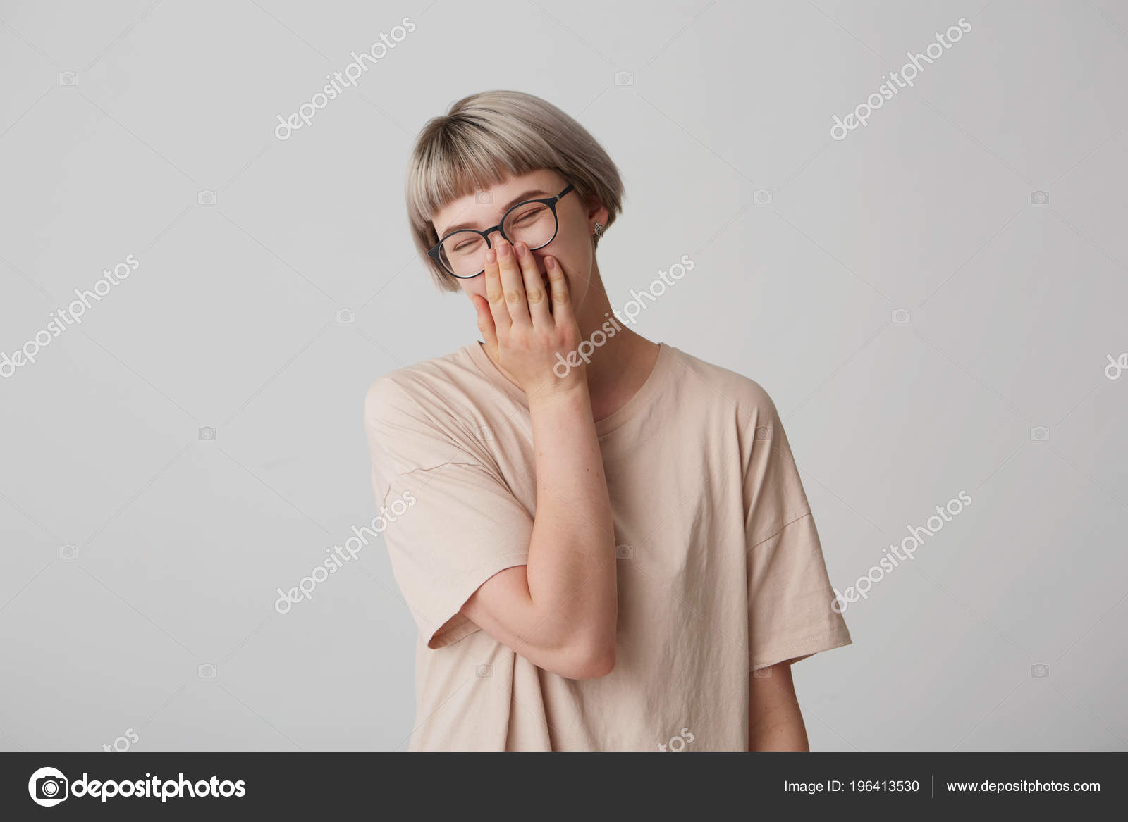 あなたはとても面白いです 若いかわいい女性の笑いの室内撮影はカジュアルなオーバー サイズ シャツと眼鏡を身に着けているし 口の中に彼女の手を保ちます 肯定的な感情 ストック写真 C Timtimphoto