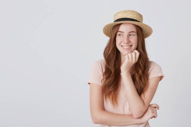 Uzun kızıl saçlı ve çilli hasır şapkalı mutlu güzel bir genç kadın çenesinin el ile yaslanır ve bir tarafı beyaz arka plan eller üzerinde seyir katlanmış