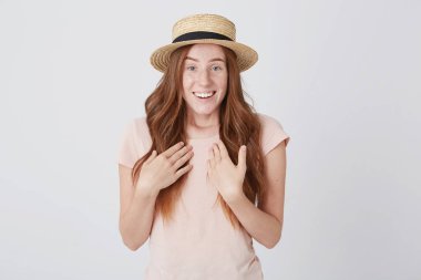 Sürpriz Kızıl genç kadın hasır şapka ve kendini işaret ve beyaz arka plan üzerinde gülümseyen tshirt closeup duygu hayran