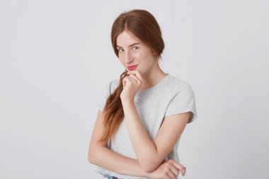 Uzun kızıl saçlı ve çilli düşünme ve gülümseyen izole beyaz üzerinde büyüleyici mutlu bir genç kadın portresi Looking kameraya arka plan