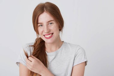 Neşeli güzel kızıl saçlı Genç kadının saçını dokunmaktan ve mutlu hissediyorum beyaz arka plan üzerinde izole gülümseyen çiller ile portre