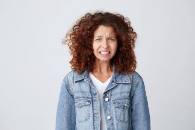 Stüdyo çekim stres duygu ve doğrudan kamera ayakta öfkeli beyaz arka plan üzerinde seyir kot ceket rahatsız kıvırcık saçlı Genç ve güzel kadın rahatsız ve kızgın