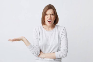 Ayakta ve beyaz arka plan üzerinde izole Palm'da boşaltmak tutarak açık ağızlı longsleeve öfkeli şok genç kadın portresi