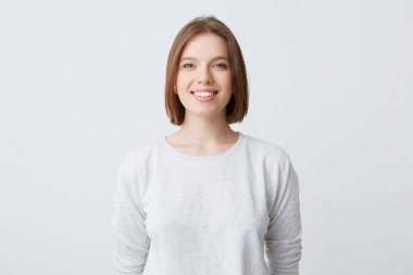 güzel bir kadın mutlu duygular ifade eder, geniş hoş gülümseme, beyaz longsleeve giyer ve memnun. Beyaz arka plan üzerinde izole