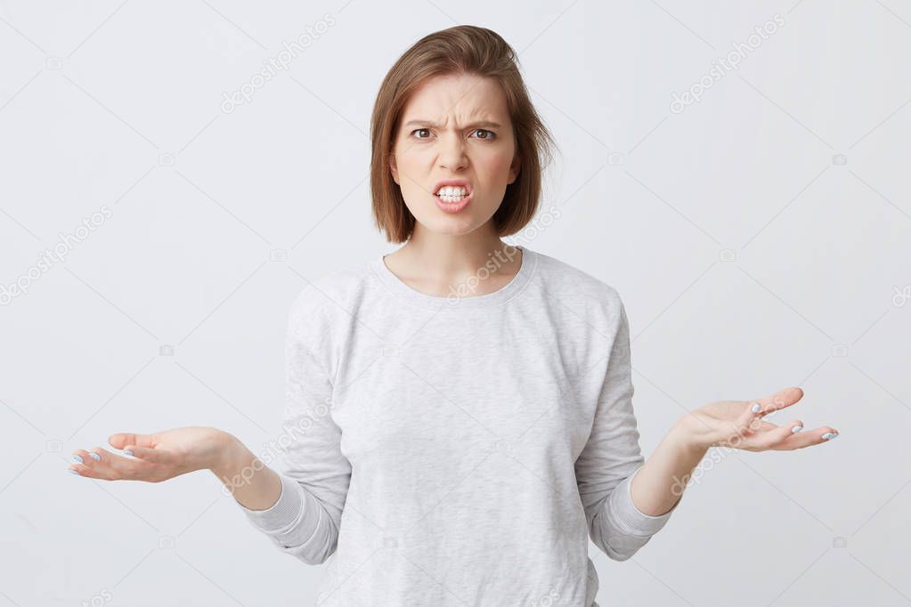 Portrait of mad irritated young woman in longsleeve feels angry and holding copyspace on both palms isolated over white background