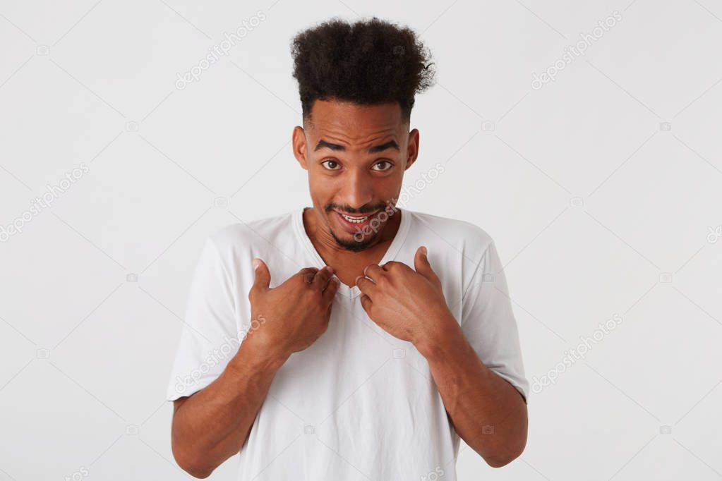 Portrait of smiling confused african american young man with afro hairstyle wears t shirt looks embarrassed and pointing on himself isolated over white background