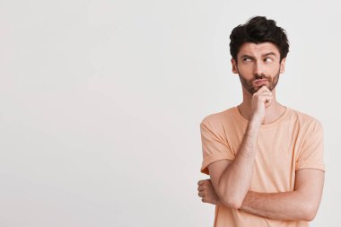 Kıl ile ciddi düşünceli genç adam portresi Şeftali t gömlek görünüyor dalgın giyer ve tutar eller izole beyaz arka plan üzerinde katlanmış
