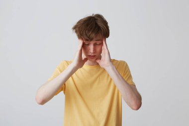 Tapınaklar dokunmaktan ve beyaz arka plan üzerinde izole baş ağrısı muzdarip sarı t gömlek genç adam üzgün closeup depresif