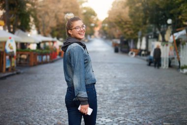 Gülüyor ve şehir sokakları, tişört ve kot pantolon, üzerinde gözlük, denim ceket giyen iyi güneşli ve güzel hava, zevk çekici genç kız yürüyüş gülümseyen açık fotoğraf için açık