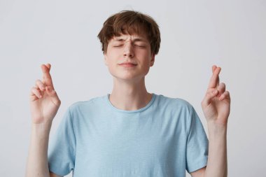 Çapraz parmak dilek, bir şey isteyen ve Tanrı'nın rüya yerine getirmek isteyen giymiş casualy beyaz arka plan üzerinde izole yaparken gözleri umutla, kapanış olumlu sadık genç bir adam,
