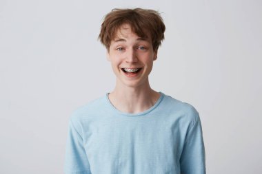 Incredibly, over-measure joyful guy smiles broadly, shows enthusiasm and passion, disheveled hair, mouth wide opened with braces on teeth, feels glad, over white background clipart