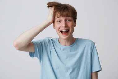 Screaming of happiness and excitement young guy clutched at his head with one hand, disheveled hair, mouth wide opened as shouting loud with braces on teeth, feels surprised over white background clipart
