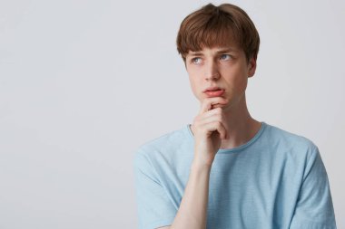 Mavi t-shirt, odaklı genç adam tutar kol çeneme ve düşünceli uzakta, şaşkın ve sorguladı, Görünüşe göre sorunu çözmek için ne düşünüyor, sıkıntılı beyaz arka plan üzerinde