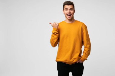 Komik mutlu mutlu yakışıklı adam, gülümsüyor, mutluluktan parlayan, tam olarak memnun, giymiş turuncu sweatshirt, kapalı fotoğraf puan boş boşaltmak parmağında başparmak ile