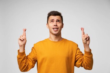 Turuncu kazak yakışıklı genç adam kafa ve kol devam ederse ve beyaz arka plan karşı dururken parmak çarpı işareti. İyi şanslar, bağışlanmak için umut isteyen. Dua, ağzını açtı