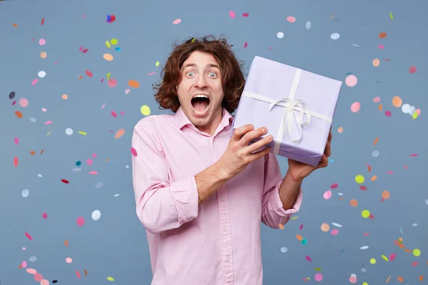 Crazy joy, great fun, happiness, inspiration feels birthday man, he received a gift box happy photographed around falling confetti on a blue background