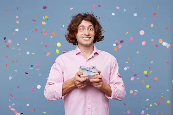 Portrait of the birthday man takes photos with a gift box, holds it in his hands, looks away, on his face an expression of bewilderment, did not expect to receive such a small gift