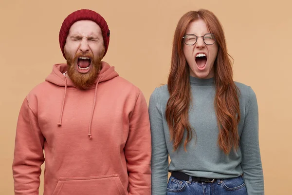 Caucasian couple, feels angry and mad, scream with widely opened mouth and closed eyes. Isolated over biege background