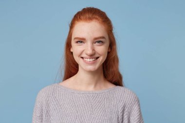 Headshot hoş gülümseyen ve mavi bir arka plan karşı izole kamera bakarak çekici neşeli Kızıl saçlı Genç kadın.