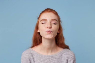 ?Ute güzel genç Kızıl saçlı kız öpücük ayakta gözleri kapalı dudaklarına bir öpücük için mavi arka plan üzerinde katlanır gönderir.