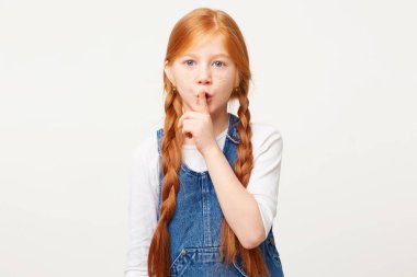 Korkmuş Kızıl saçlı çocuk iki örgüler ile ön plana tutan parmak dudaklarından, komplo tutmaya çalışıyor, kamera görünüyor, diyor ki: sus, sessizlik lütfen olun.' Kızın izole atış sessizlik jest gösterir