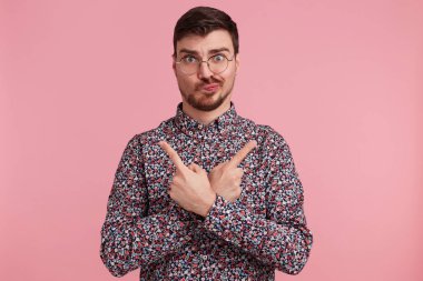 Genç adam şüpheleri düşünce gözlük arıyorum renkli gömlek ve karıştırmayın yüz ifadesi ile çapraz eller Toplom bouth taraf için pembe arka plan izole inde parmaklarıyla işaret tutar
