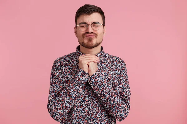 Young male student keeping his fists crossed and closed eyes with hope making a old wish. Charming nice positive guy sincerely believing in his luck, in victory of team over pink background — Stock Photo, Image
