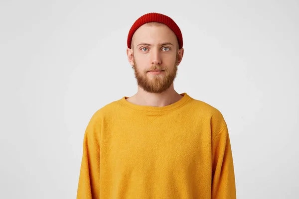 Atractivo joven en el estudio mirando camera.Calm interesante tipo hipster barbudo en sombrero rojo con expresión de la cara normal, sobre fondo blanco. Hombre toma foto para pasaporte en estudio local — Foto de Stock