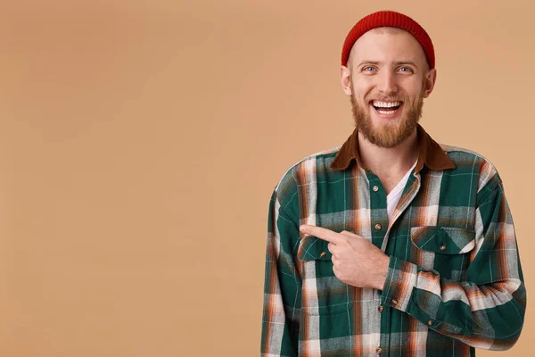 Perky and cheerful happy interesting bearded guy smiles broadly and laughs, shows with his index finger to the left to an empty space for advertising. — Stock Photo, Image